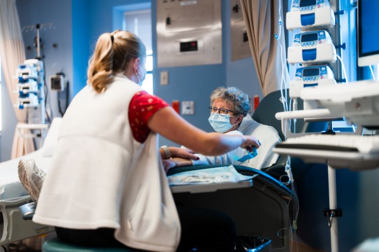 A female patient wearing a mask receives chemotherapy administered by a nurse.