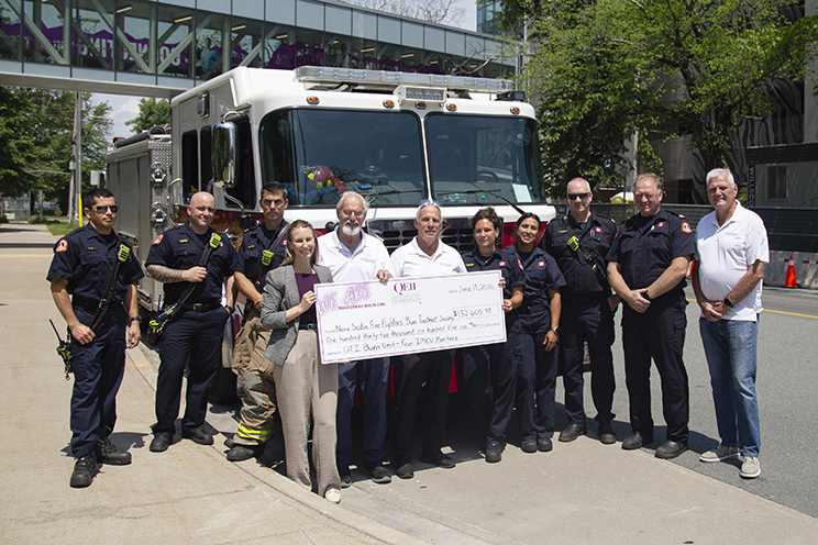 A group of Nova Scotia firefighters stand in front of a fire truck, present a cheque tot the QEII Foundation.