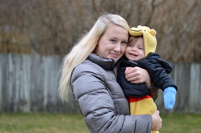 A woman, holding her baby, smiling towards the camera. 