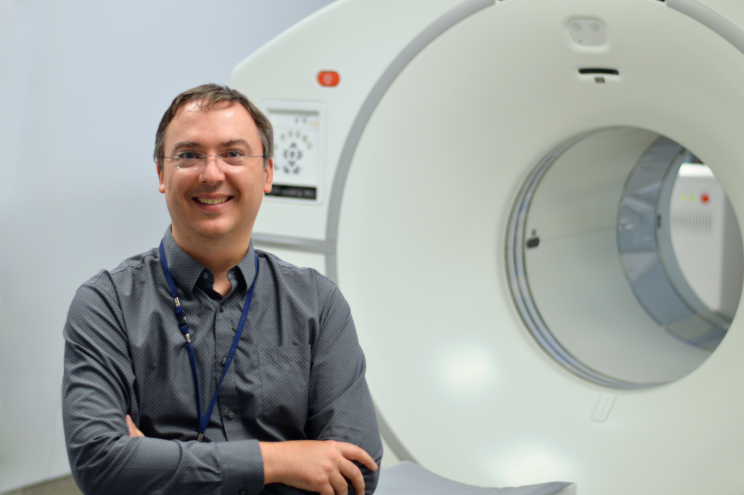 A doctor in front of an MRI machine smiles at the camera. 