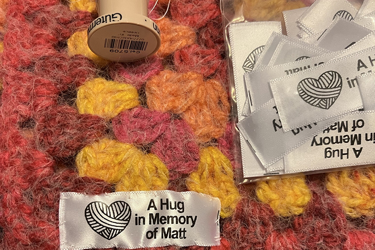 A red, orange and yellow blanket with a tag that reads "A hug in memory of Matt."