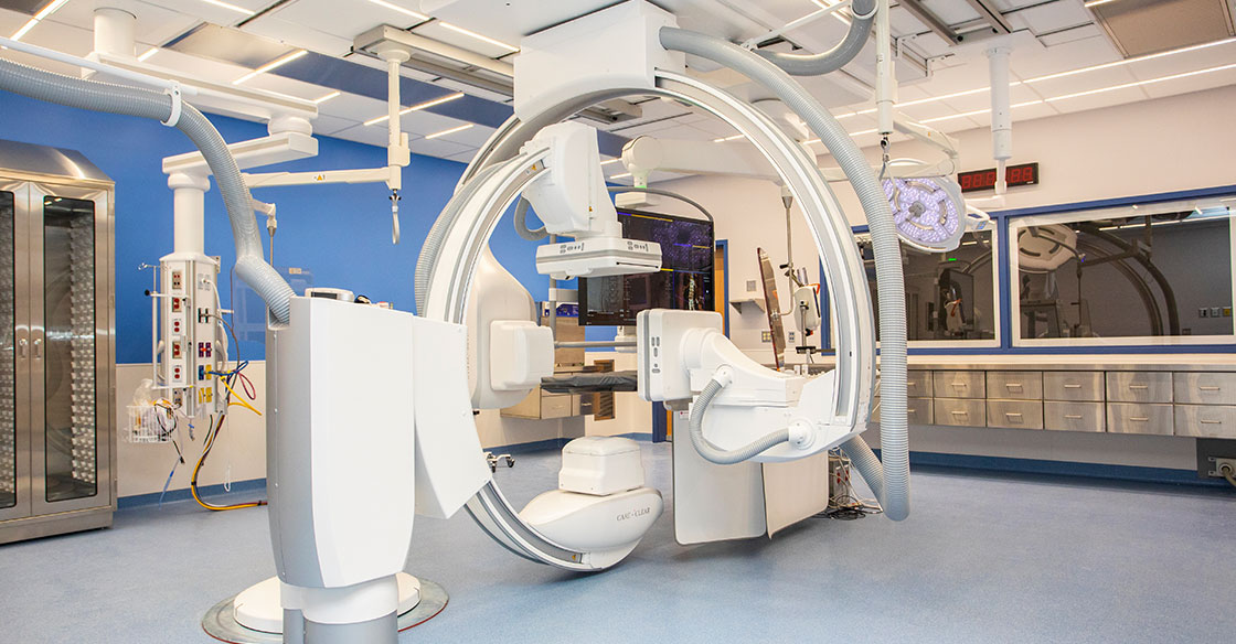 Photo of the QEII's IR suites; a white procedure room featuring a medical c-arm and bed for interventions.