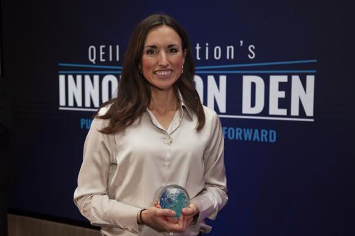 A woman, holding a circular glass ball that is an award, smiles at the camera. 