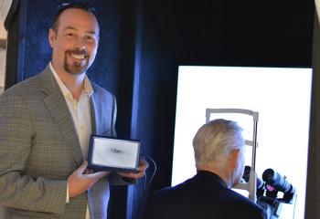 Charles Rutt looks into the glaucoma detection device, Dr. Brennan Eadie displays the image of Charles’ eye on a hand-held screen.