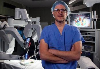 Surgeon, Dr. Ricardo Rendon, wears blue scrubs and glasses while standing in an operating room alongside the da Vinci surgical robot.