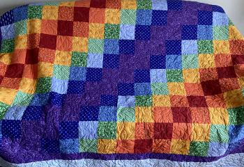 A large rainbow coloured quilt adorned with a hand-stitched rose pattern