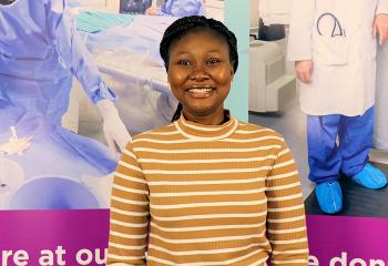 Yemisi smiles and stands proudly in front of a QEII Foundation backdrop