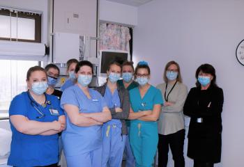 CCU team, all wearing scrubs and masks, stand in a hospital room with their arms crossed