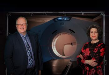 Two cancer care experts stand in front of the QEII's CT simulator machine, which resembles a CT scanner