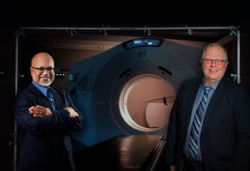 Two cancer care experts stand in front of the QEII's CT simulator machine, which resembles a CT scanner