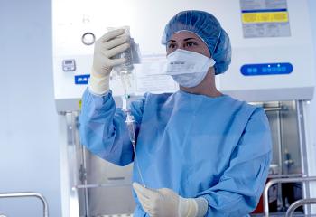 A woman dressed in blue scrubs holds up a medical vial