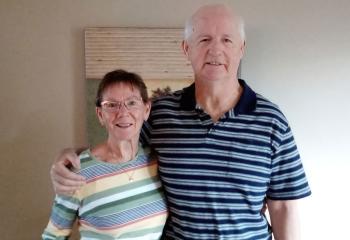 Older couple stands in front of beige wall and painting