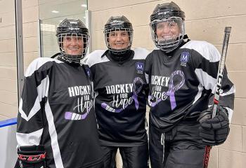 Three women standing together, wearing hockey gear