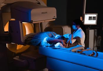 A person lies in a medical scanner, with a healthcare provider to the right of the scanner preparing the patient for the procedure. 