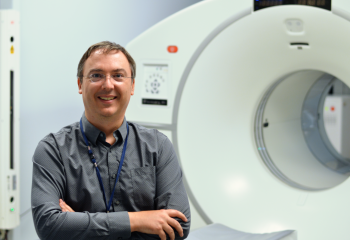 A man stands in front of a diagnostic imaging machine in a healthcare setting. 