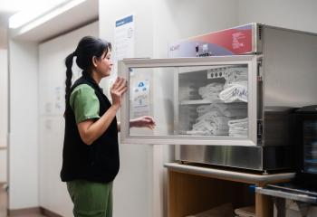 A nurse reaches into a machine that holds warm blankets. 