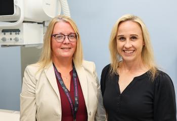 Two women stand in front of the  newly acquired Precision 180 Fluoroscopy Unit at the QEII’s Rehab Centre. 