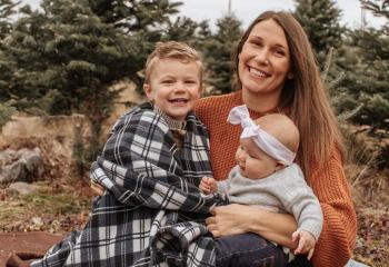 Erin Van Dusen sits at the edge of a forest with her two small children.