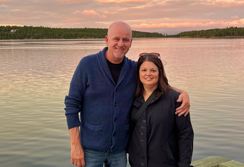 Kevin Rainey and his wife pose in front of a sunset lit lake 
