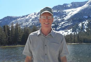 Rob stands in front of lake with mountains in backgroudn