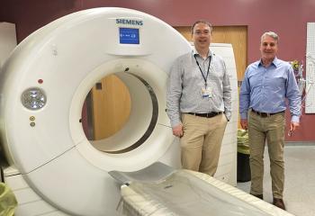 Two QEII specialists stand beside the old CT scanner to be replaced by the PCCT.