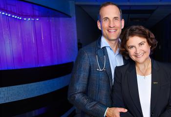 Drs. Rutlege and Ilie pictured in front of purple wall in the QEII Cancer Centre