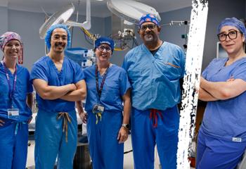 Five QEII anesthesiologists in blue scrubs pose for the camera in an operating room.