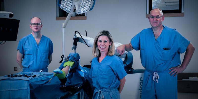 Dr. Glen Richardson, Janie Wilson, PhD and Dr. Michael Dunbar stand with the orthopaedic surgical robot.