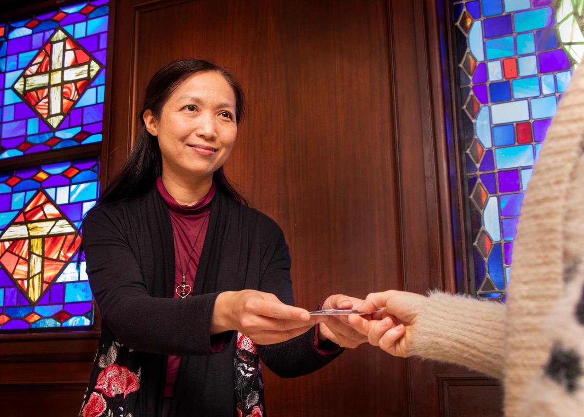 A woman, smiling, extends a gift card to a person whose hand is also extended, but face is not shown. 