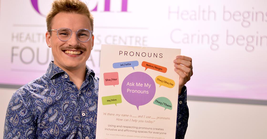 Garry Dart wears a blue patterned shirt and smiles holding up a pronouns poster
