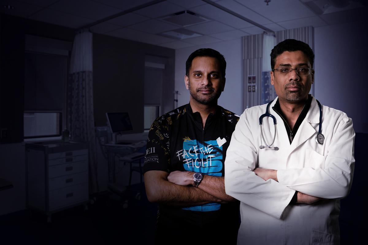 Two males looking towards the camera with slight smiles. The male on the left wears a cycling jersey. The male on the right is in a white coat and stethoscope around his neck.
