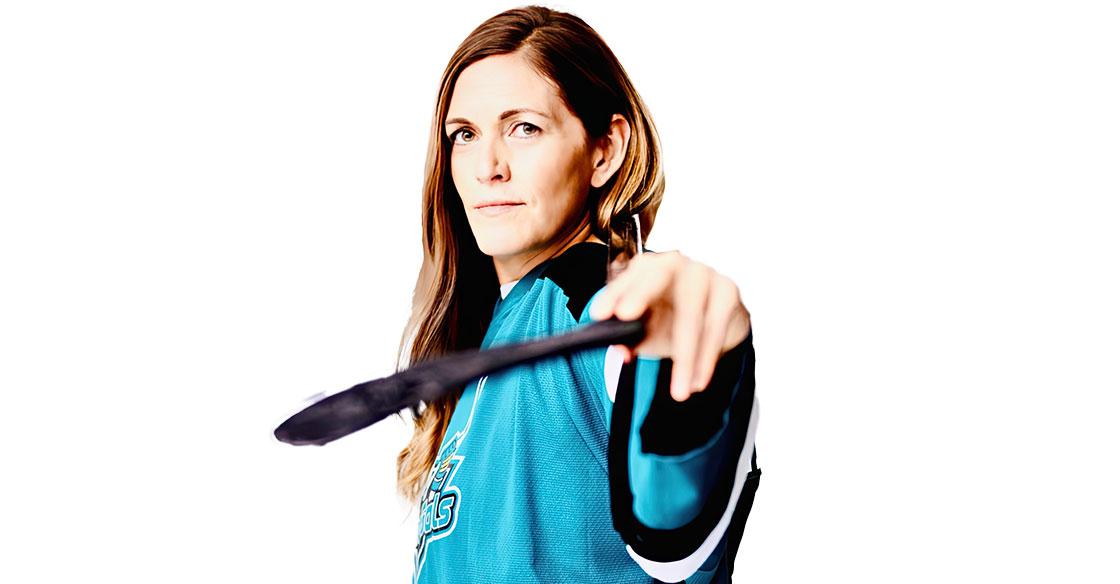 Young woman in blue jersey, posing with hockey stick