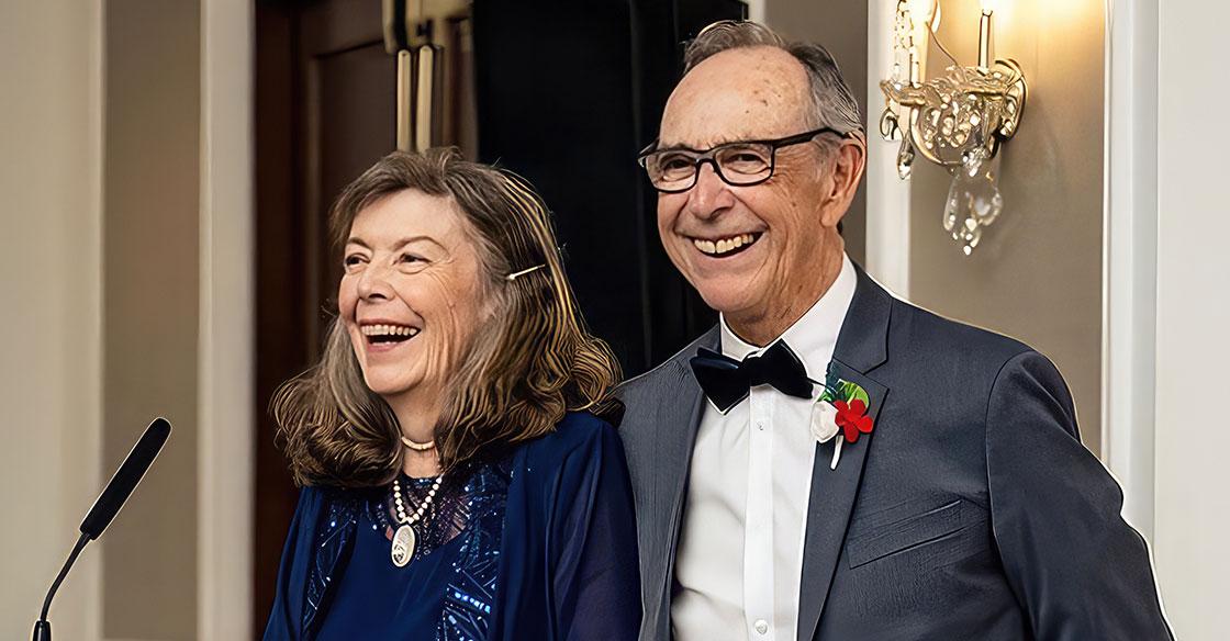 Couple standing a microphone at their child's wedding, beaming with pride