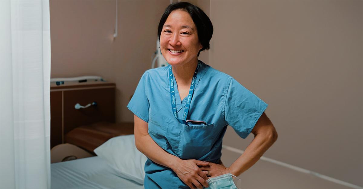 Physician wearing blue scrubs, standing in patient care area