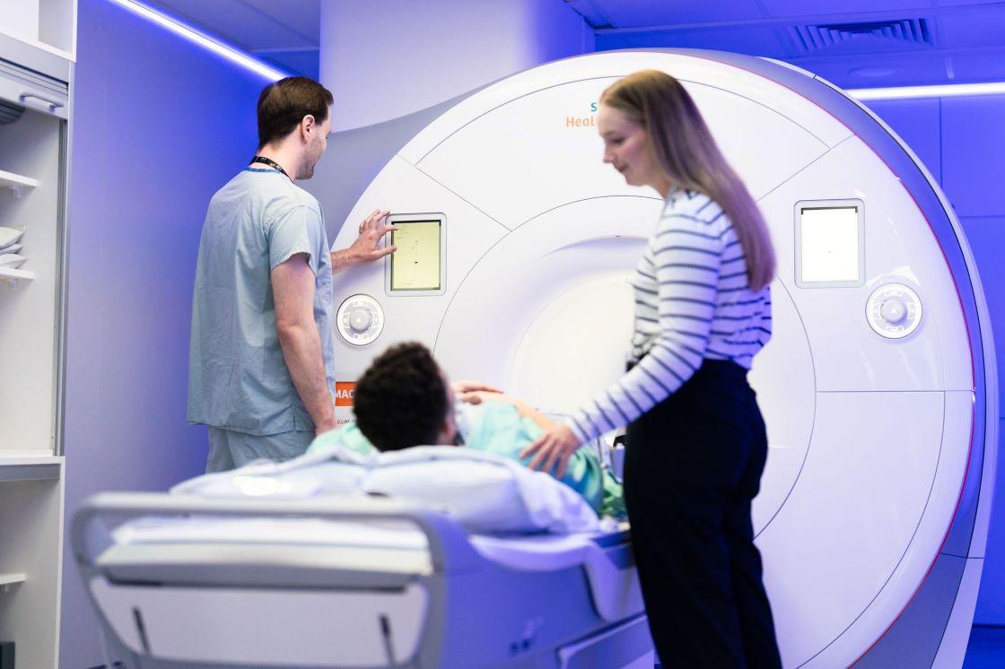 A patient prepares to have an MRI scan with the assistance of two medical professionals. 