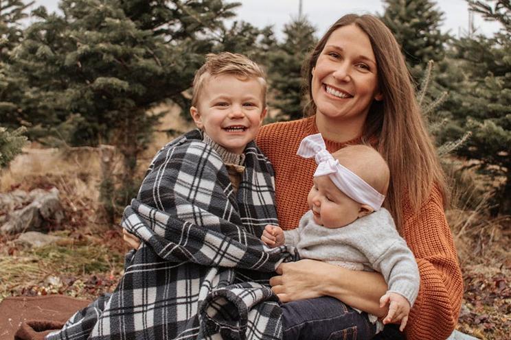Erin Van Dusen sits at the edge of a forest with her two small children.