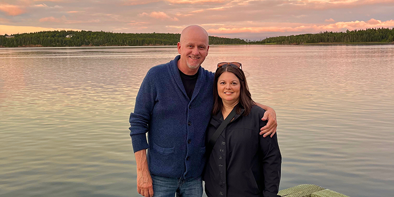 Kevin Rainey and his wife pose in front of a sunset lit lake
