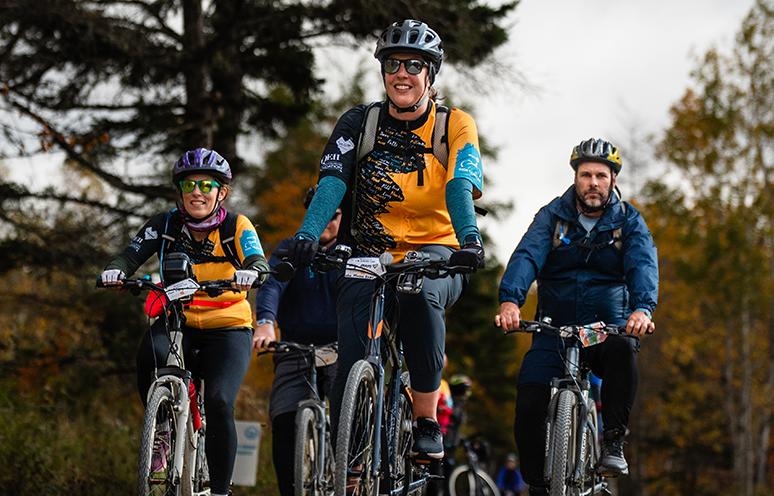 Three people dressed in BMO Ride for cancer jerseys ride there bikes on the trail during the 2025 event.