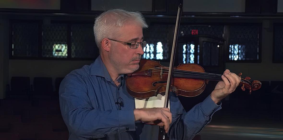 Renaud plays a violin with a church background. 