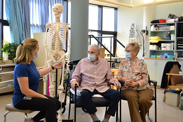 A QEII physiotherapist uses an anatomical skeleton to show a patient and his wife the site of is injury.