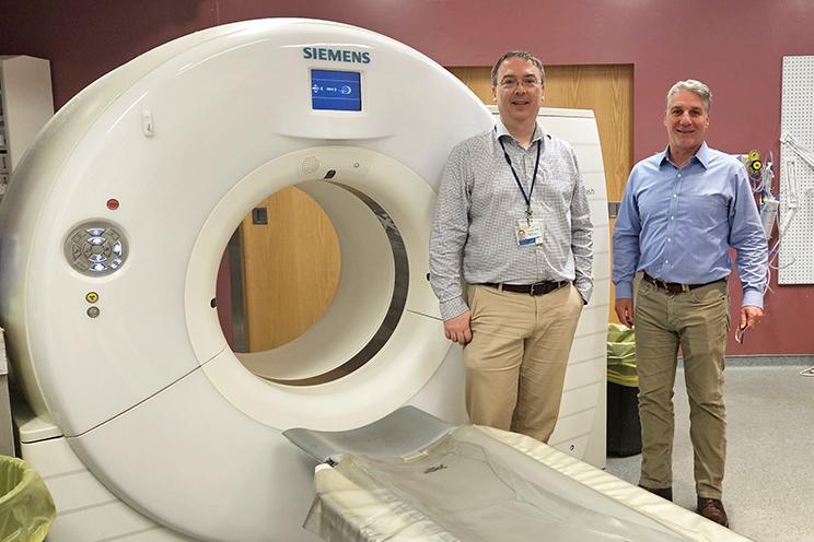 Two QEII specialists stand beside the old CT scanner to be replaced by the PCCT.