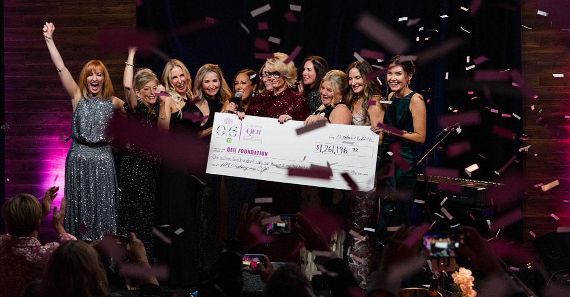 On-statge cheque presentation photo with confetti and celebrating more than $1.2M raised