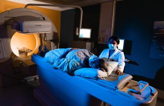A female patient is laying down, preparing to undergo a medical scan. A female healthcare professional stands close to the patient. 