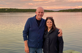 Kevin Rainey and his wife pose in front of a sunset lit lake 