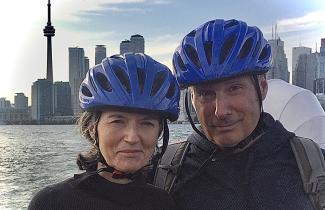 A couple wearing bicycle helmets pose in front of the Toronto skyline.