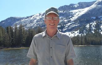 Rob stands in front of lake with mountains in backgroudn