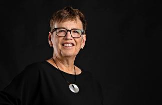 Susan Mullin, CEO at the QEII Foundation, poses for the camera on a dark background.