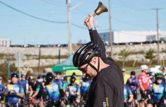 A rider wearing a black shirt and helmet rings a bell in front of a large crowd