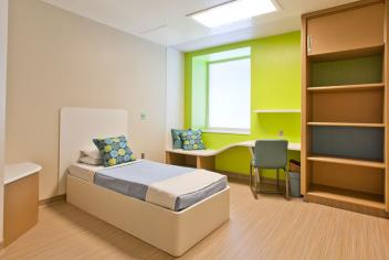 A bright, modern seclusion room featuring a bed and book shelf.