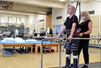 Barry Pettipas stands in the body weight support system with the help of a QEII physiotherapist